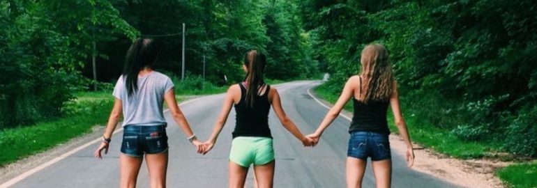 3 girls standing in the middle of the road holding hands