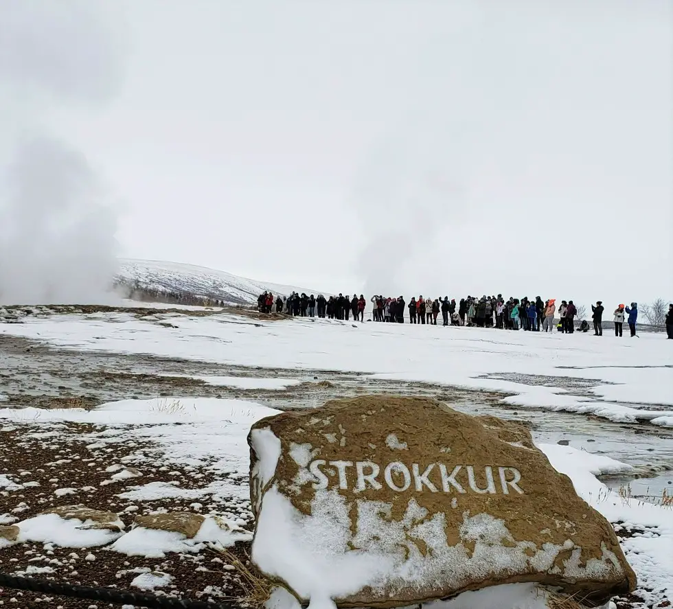 crowd of people around steaming Strokkur geysir in Iceland along Golden Cirlce driving route