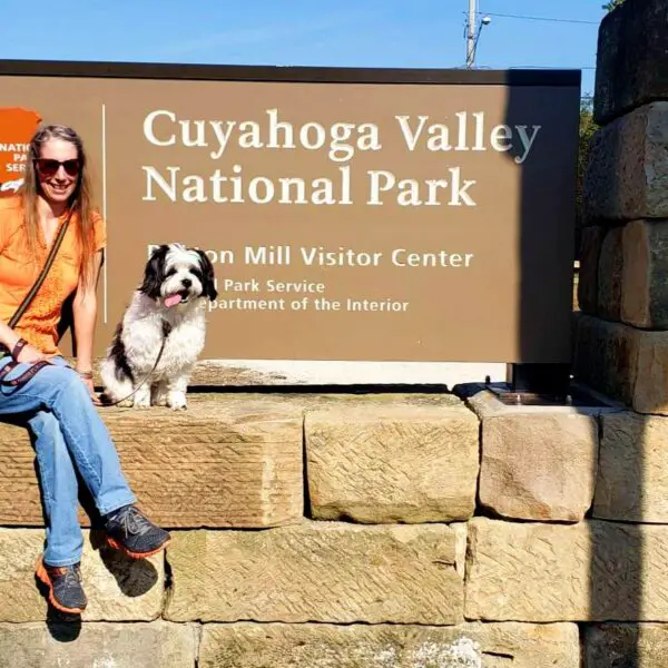 lady and dog sit at the Cuyahoga Valley National Park sign