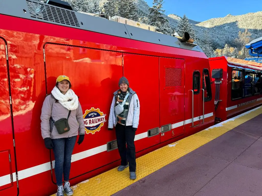 2 ladies standing in front of a red rail car on their way to Pikes Peak