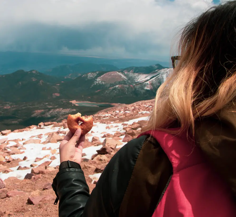 woman holding donut at the top of Pikes Peak