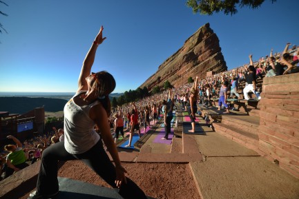 woman stretching in yoga pose in from of lots of people doing yoga at red rocks in denver colorado