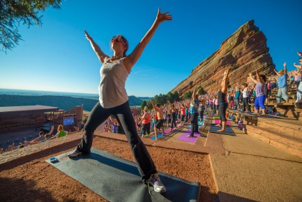 woman stretching with arms outstretched in yoga pose in from of lots of people doing yoga at red rocks in denver colorado