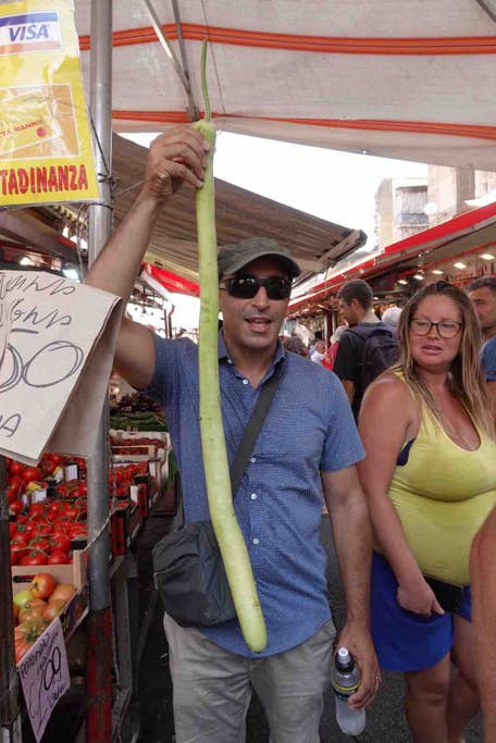 man holding up a long zucchini at a Palermo street food market