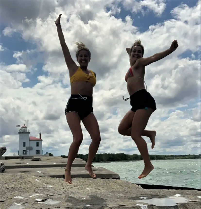 2 girls jumping on the rocks in front of the lighthouse near headlands park state beach near lake erie