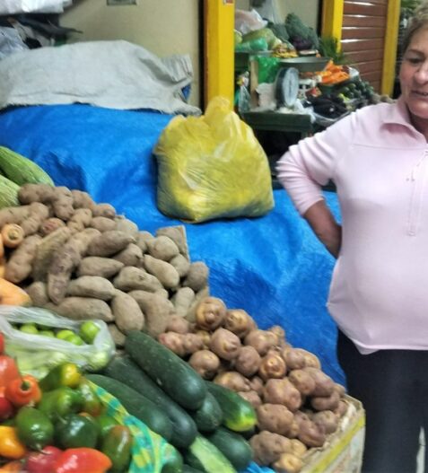 Lady standing with all the potatos and typical food of Peru