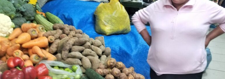 Lady standing with all the potatos and typical food of Peru