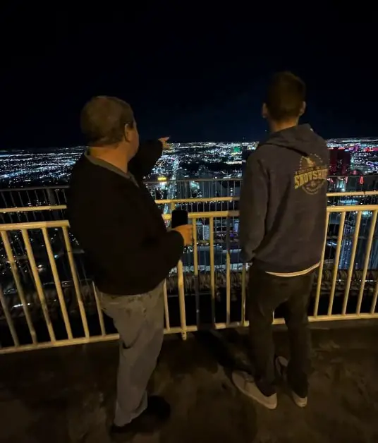 2 guys pointing at the view of all the lights in las vegas from the top of the stratosphere