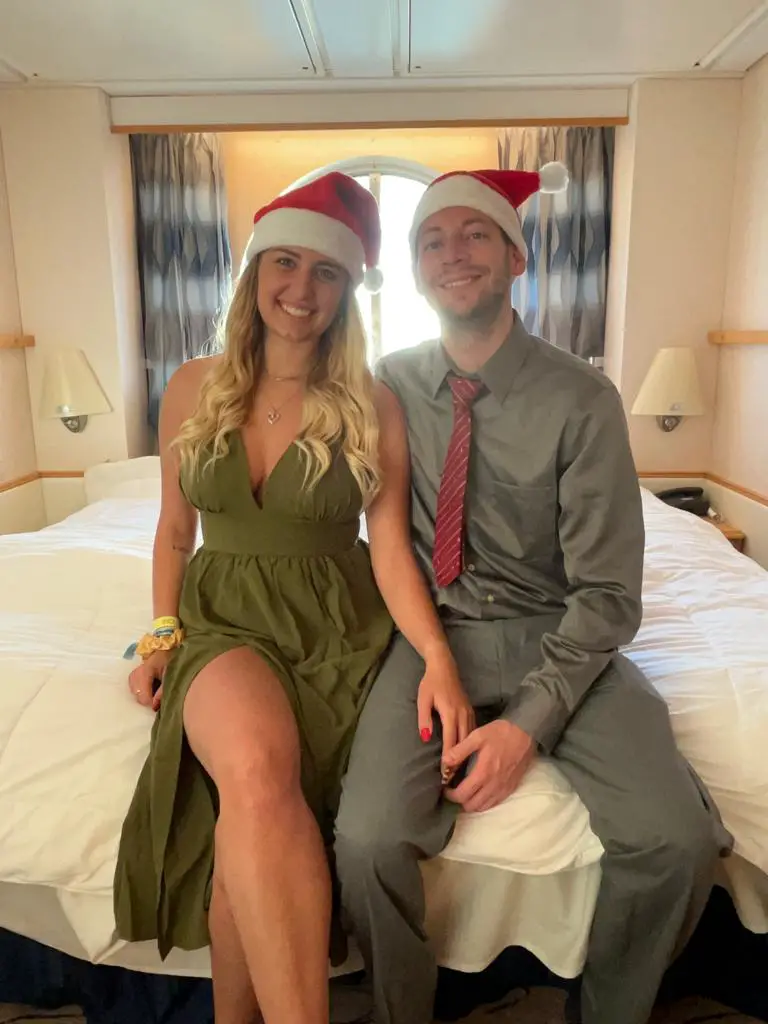 2 people in santa hats sitting on a bed in front of a window