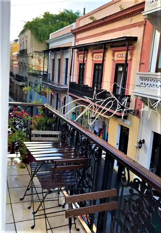 small table and chairs on a balcony overlooking a street in old San Juan with colorful historic buildings