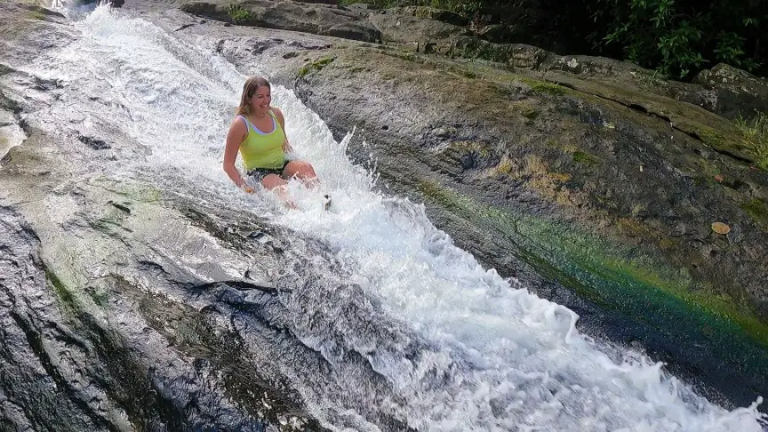 girl in a tank top sliding down a waterfall on a natural slide in puerto rico
