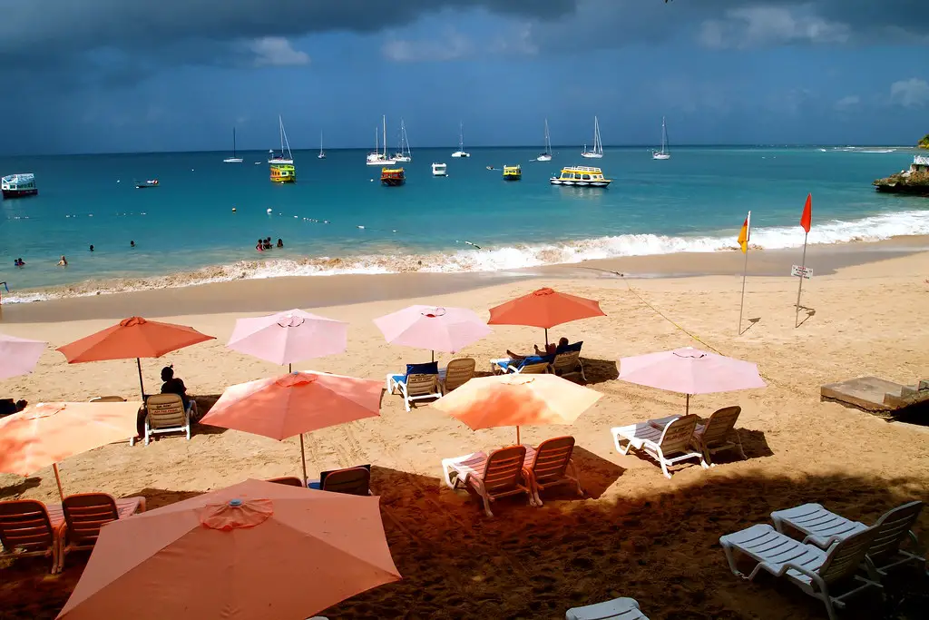 many beach chairs and umbrellas on the beach and boats in the water at the best beach in Tobago Store Bay