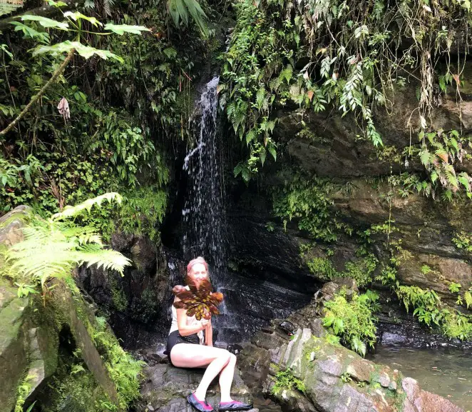 lady sitting on a rock in front of a waterfall on a day trip while visiting el yunque on your own