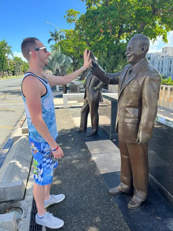 man standing with hand outstretched to a bronze statue at the walkway of presidents in old san juan puerto rico