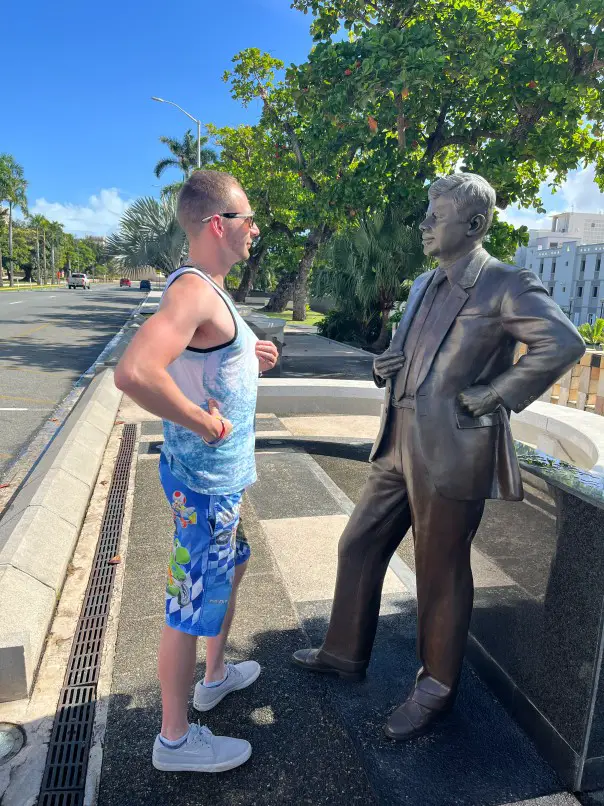 man standing with hand on hip on front of bronze statue at the walkway of presidents in old san juan puerto rico