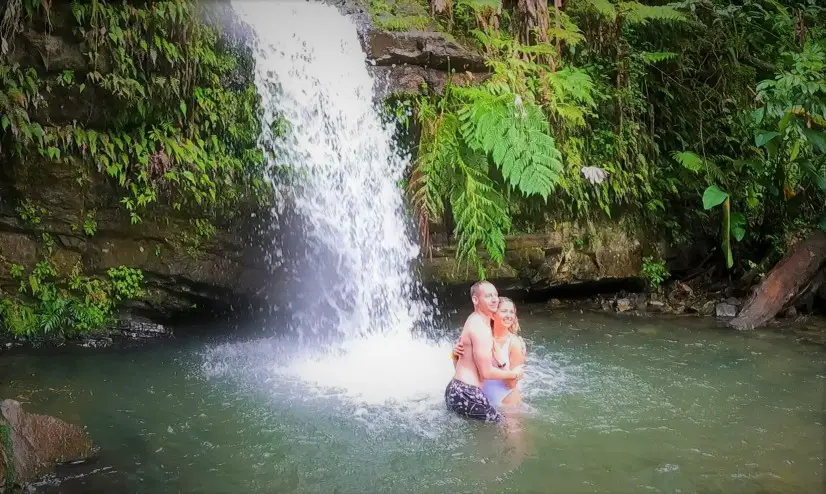 couple posing in water in front of a Waterfall at Juan Diego Creek is one of the best things to do in El Yunque Rainforest