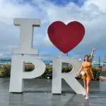 girl standing with her arms out in front of the I love PR sign - taking photos during our 3 days in Puerto Rico