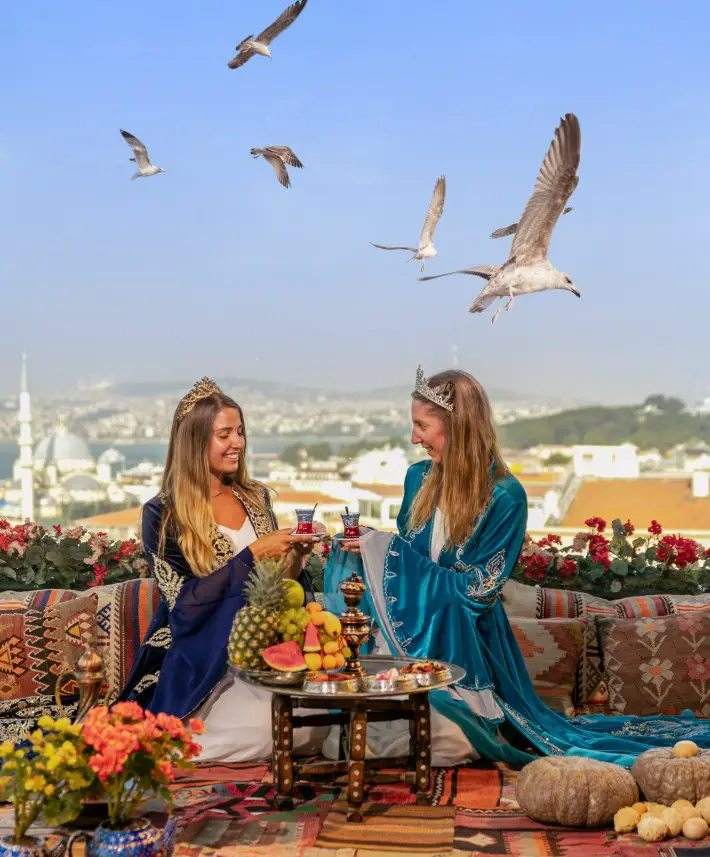2 ladies sitting at the best rooftop view in Istanbul with birds flying over and the city in the background