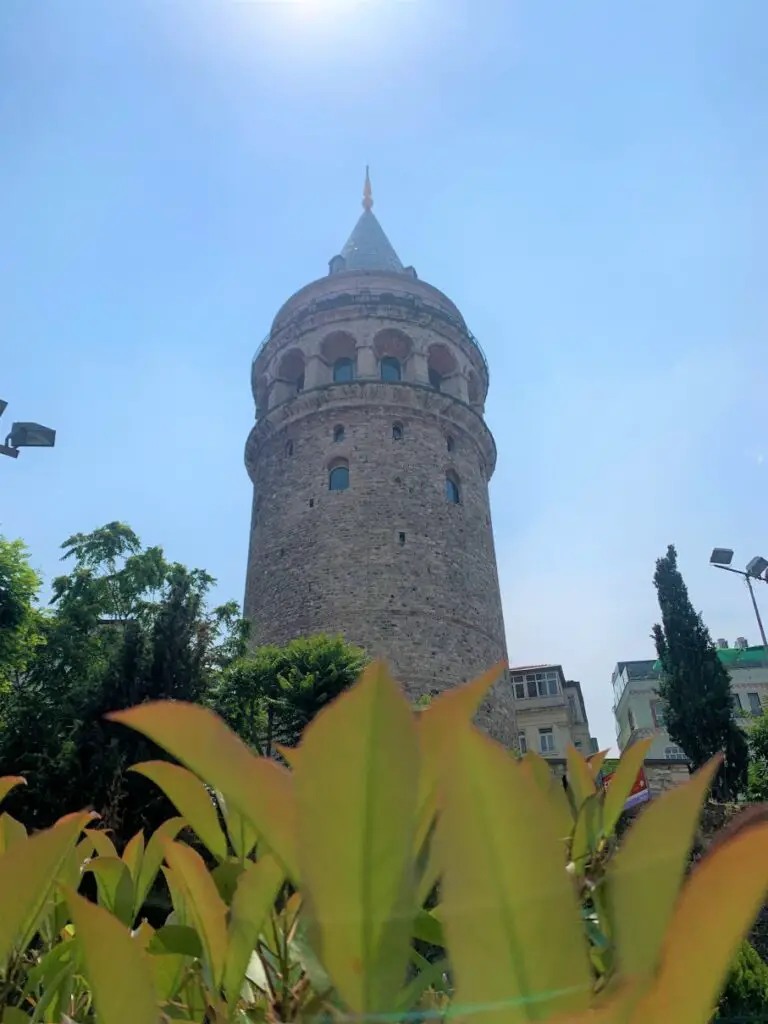 Galata Tower in Istanbul rising into the sky behind some flowers and greenery