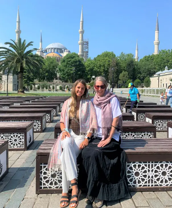 2 ladies sitting on a bench in front of a mosque in Istanbul taking in the best photos in Istanbul