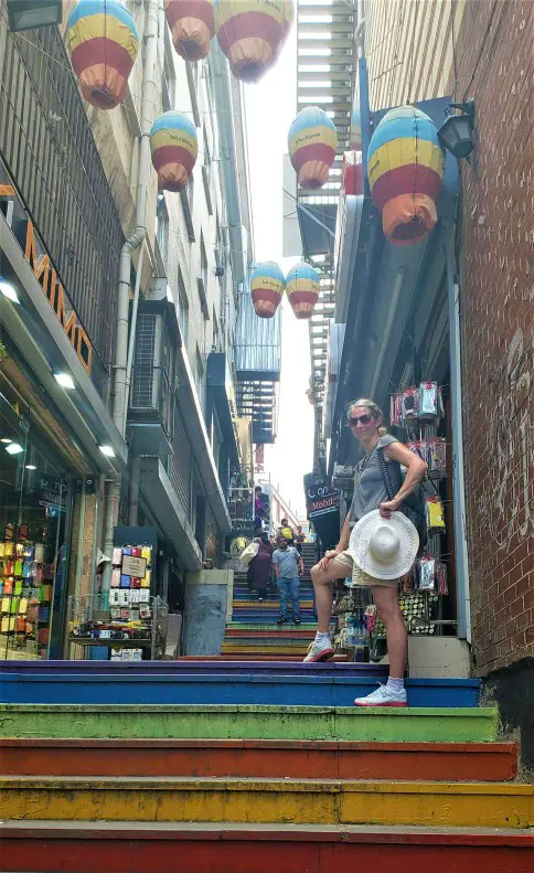 lady standing on rainbow colored stairs in Istanbul with shops on the sides of the stairway