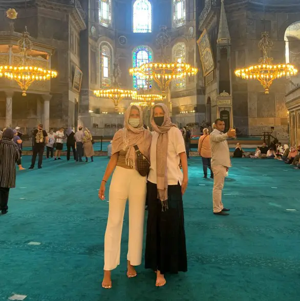 2 ladies in the middle of a mosque wearing head coverings, masks and without shoes in Istanbul Turkey