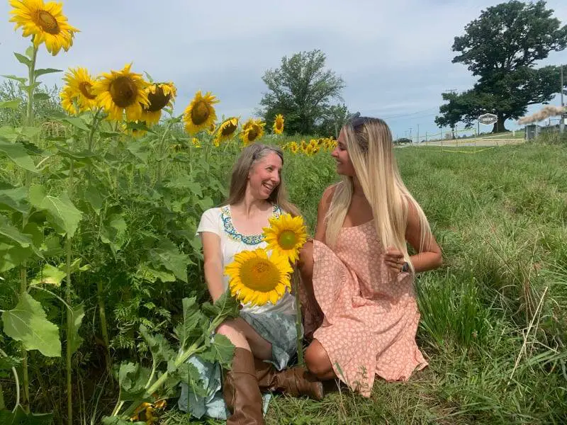 two ladies sitting in a sunflower field as an example of cute ideas and outfits to wear in a sunflower field