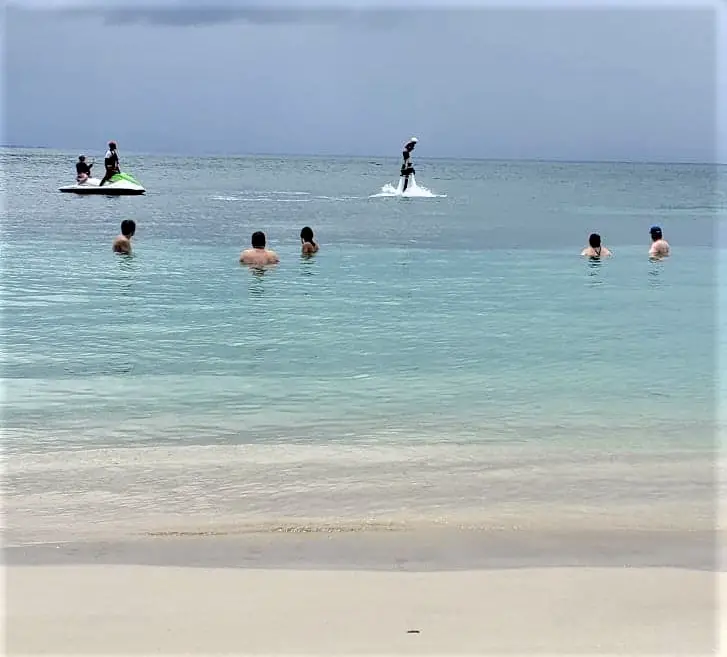 a few people swimming and one person attached to a jet ski with a power jet on the beach in st kitts