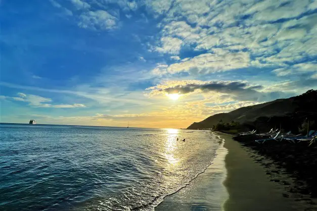 golden sunset over the water with a boat in the distance at one of the Best Beaches in St Kitts - Sunset on Shipwreck Beach