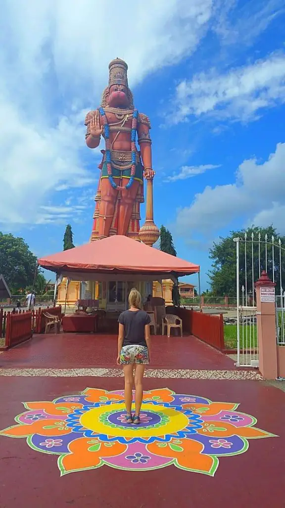 lady standing in front of a very tall and colorful Hanuman Murti statue at Dattatreya Yoga Center in South Trinidad