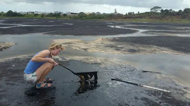 lady scooping up some black substance at Pitch Lake in La Brea as one of the fun things to do in South Trinidad