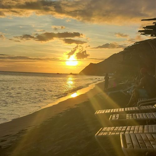 Golden rays of the Sunset shining down on the lounge chairs and sandy beach at Shipwreck Beach in St Kitts