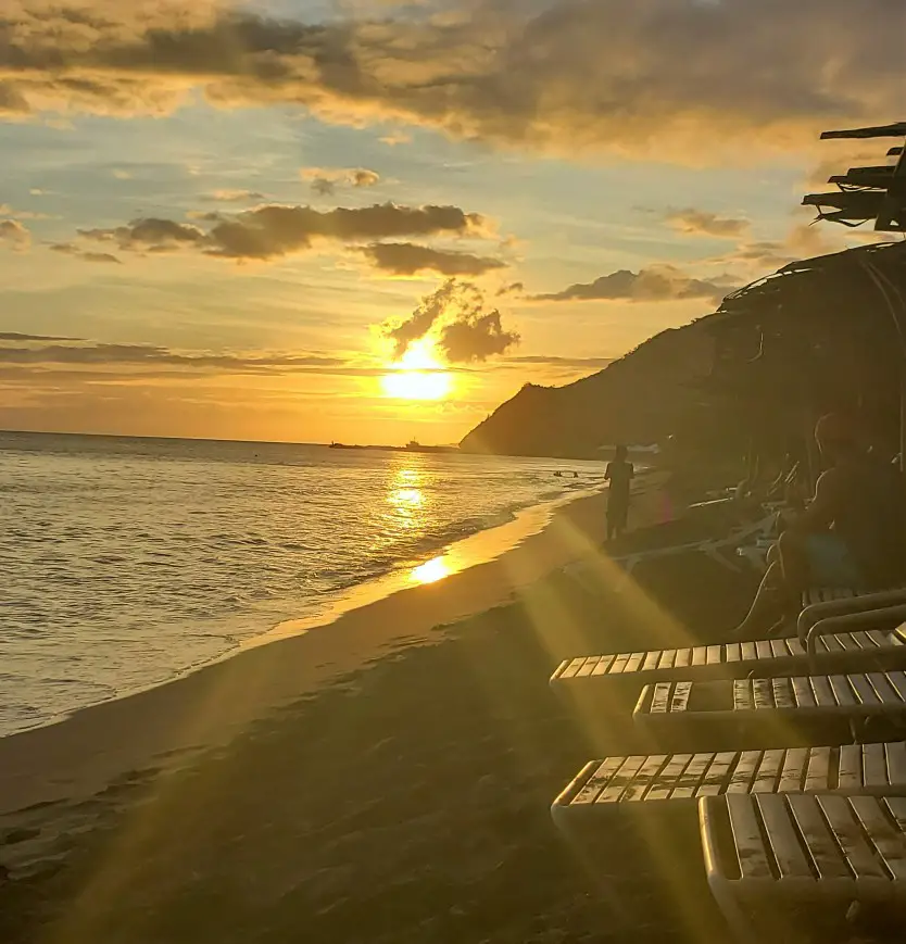 Golden rays of the Sunset shining down on the lounge chairs and sandy beach at Shipwreck Beach in St Kitts