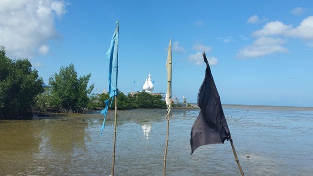 3 flags in the foreground and Temple in the Sea in the distance in Trinidad