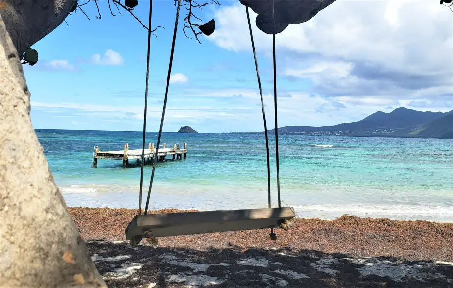 looking through a swing onto a mossy, sandy beach with a boardwalk out in the middle of the water in st kitts