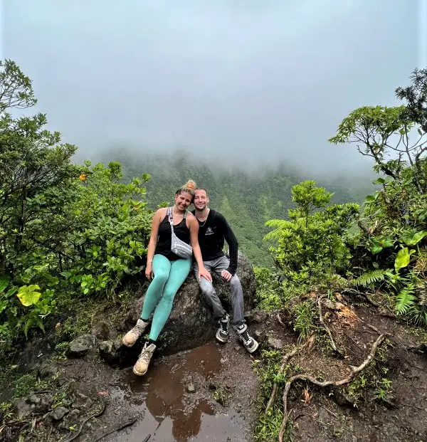 2 people sitting on a ledge with mist surrounding them at the top of volcano Mt Liamuiga view