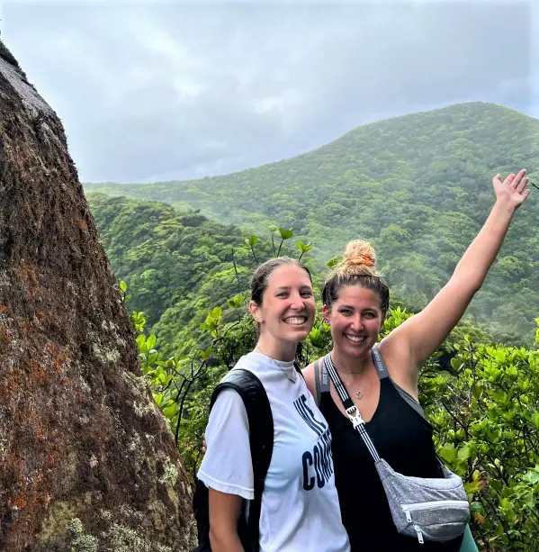 girl standing with an outstretched arm at the top of volcano after hiking up Mt Liamuiga