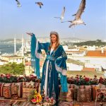lady standing in a velvet cloak with arm raised toward seagulls llying above at a Rooftop Photo shoot in Istanbul with seagulls
