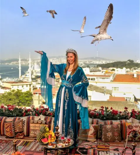 lady standing in a velvet cloak with arm raised toward seagulls llying above at a Rooftop Photo shoot in Istanbul with seagulls