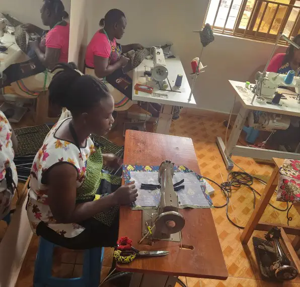 local women sit at sewing machines for Creating designs in kampala slums