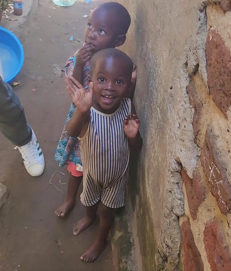 small child with no shoes smiling and waving in kampala slum