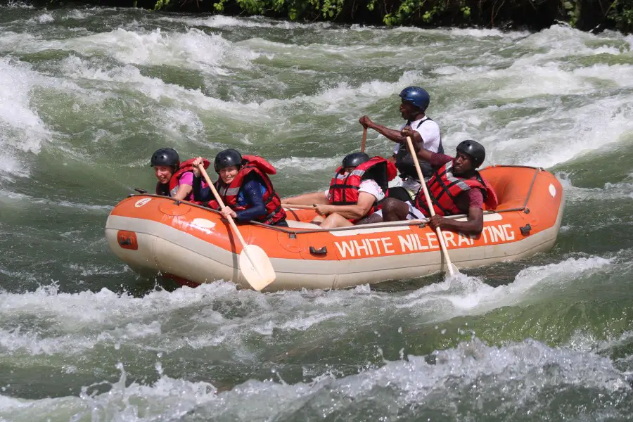 orange raft boat in rapid with people paddling in life jackets on the Nile river in uganda on a day trip from kampala