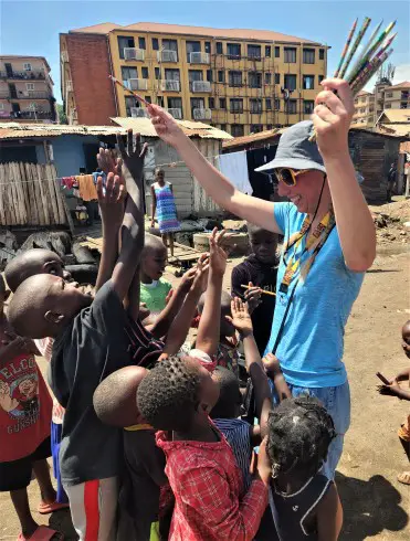 children raising their hands to grab a pencilin the slum in kampala