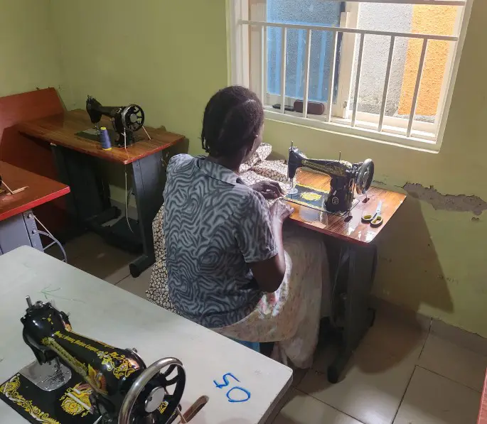 ladysits at sewing machine - local seamstress in Kampala slum