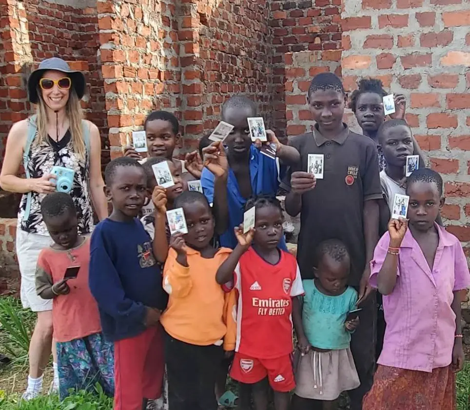 children holding up their photos in front of an abandoned brick building in the slums in uganda