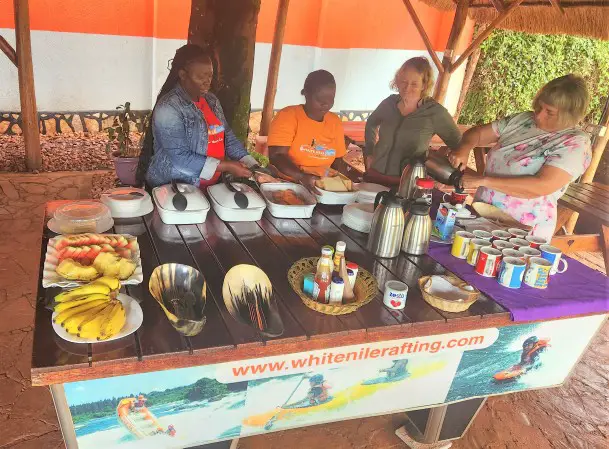Ladies standing at a table with a lot of food and fruits for breakfast before going white water rafting in Uganda on the Nile