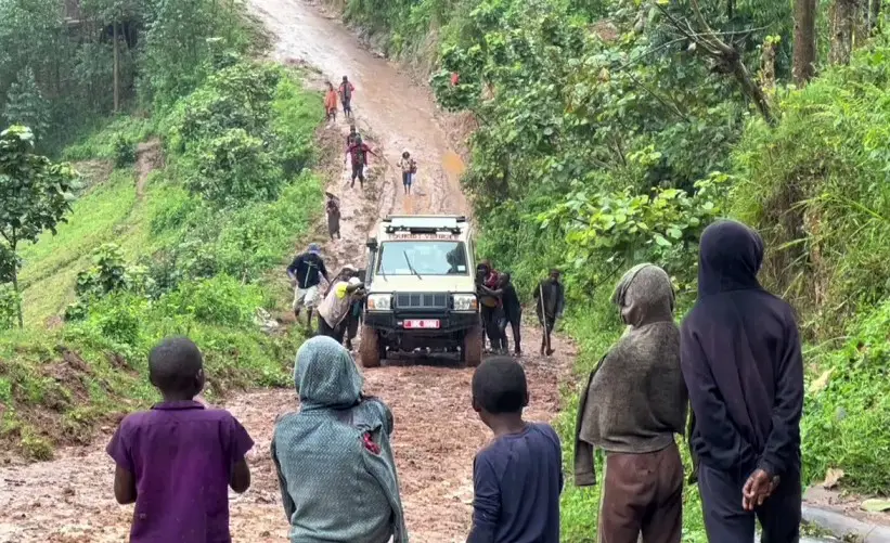 lots of people pushing a car and onlookers watch down the hill at the car getting stuck on a hill in Bwindi in Uganda