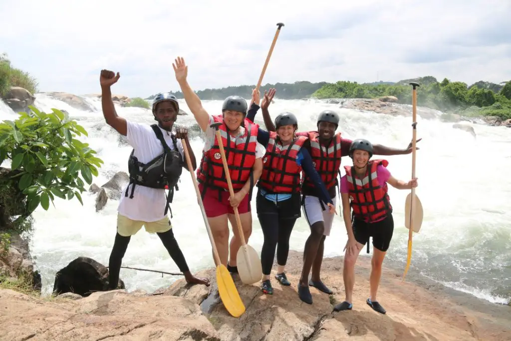people with paddles in the air in front of the water posing in front of class 6 rapid on our Uganda white water rafting trip