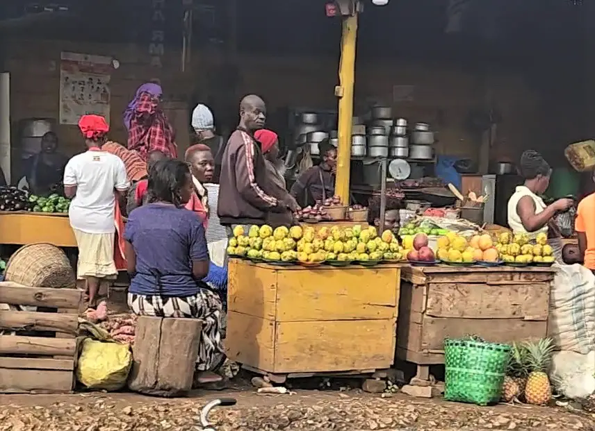 lot of fruit and produce stack on tables as Villagers are shopping on the streets in Uganda