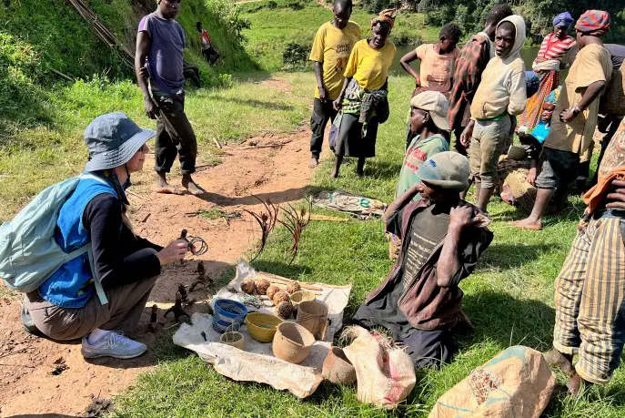 lady kneeling at a tarp surrounded by people and shopping with Batwa locals in Uganda